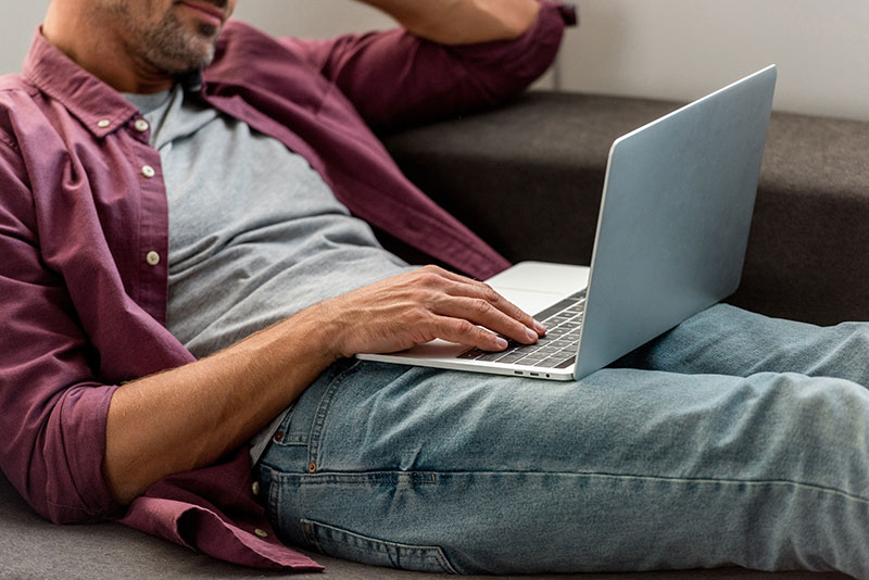 Mann sitzt auf Couch und tippt auf Laptop