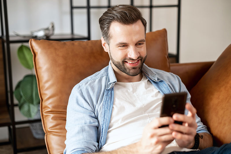 Mann sitzt auf Couch mit Smartphone in der Hand