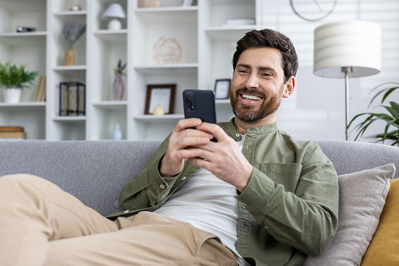 Mann sitzt mit Handy auf der Couch und lacht