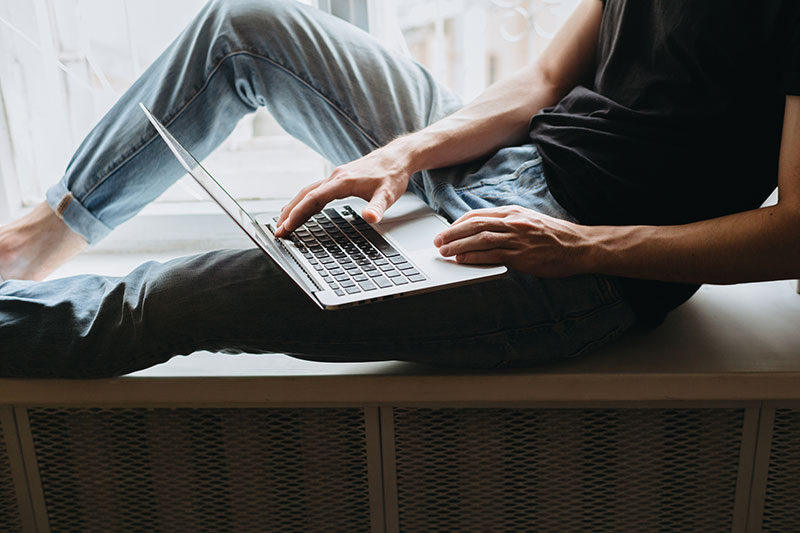 Mann sitzt mit Laptop auf der Fensterbank