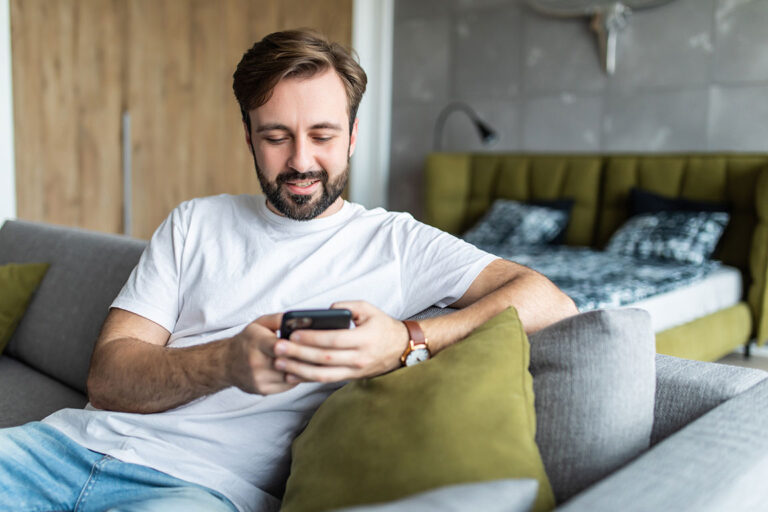 Bärtiger Mann sitzt mit Handy auf dem Sofa