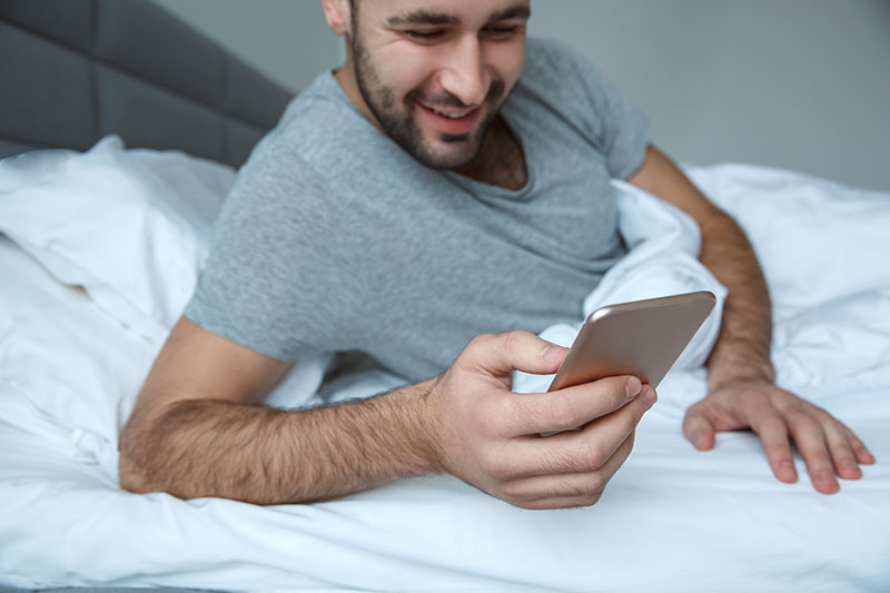 Mann schreibt am Smartphone eine Nachricht im Bett