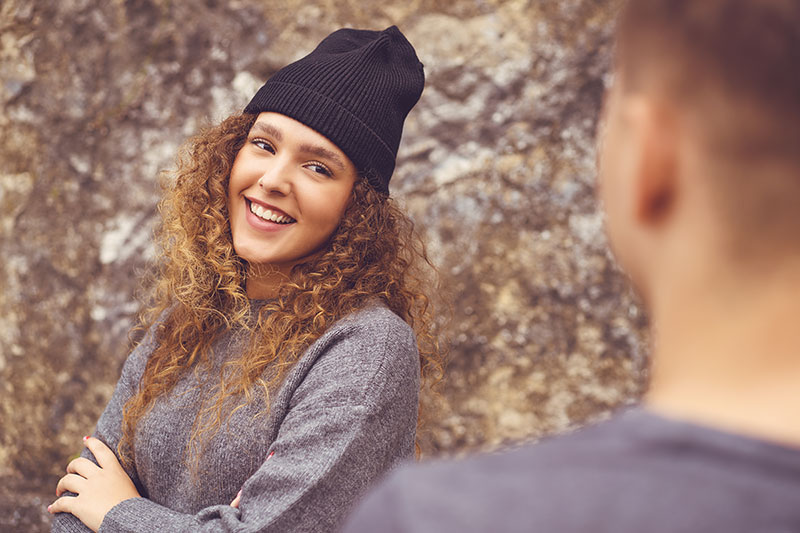 Frau mit lockigen Haaren und Strickmütze lächelt Mann an