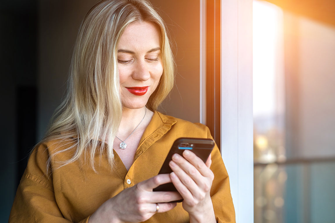 Blonde Frau mit rotem Lippenstift schaut fröhlich auf ihr Smartphone