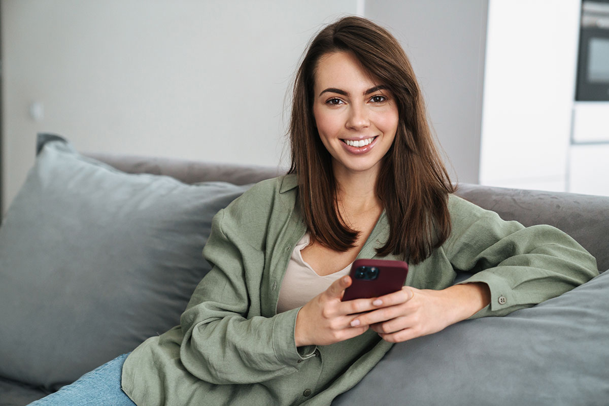 Brunette Frau lächelt mit Handy in der Hand