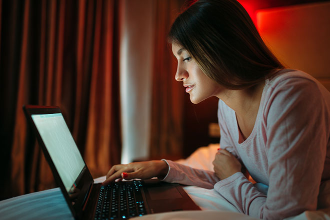 Frau liegt im Bett und schaut auf Laptopbildschirm