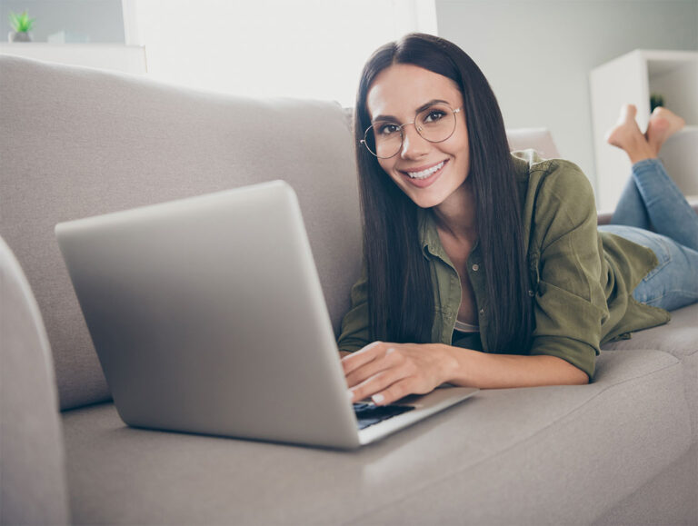 Frau mit Brille liegt auf Couch mit Laptop