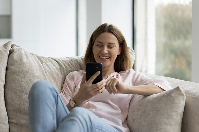 Frau sitzt auf Sofa mit Smartphone und lacht