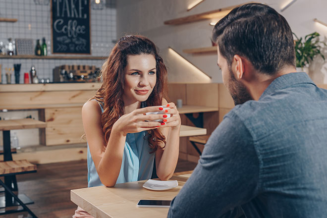 Frau sitzt in einem Cafe und schaut Mann aufmerksam ins Gesicht