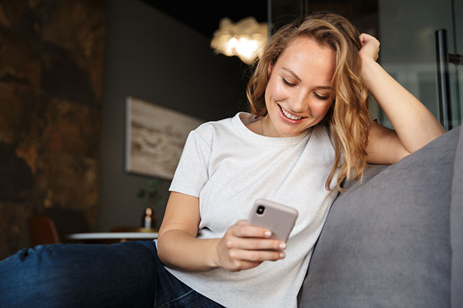 Glückliche junge Frau mit Handy auf dem Sofa