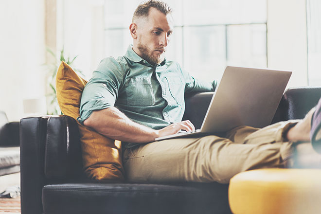 Mann sitzt mit Laptop im Schoß auf der Couch