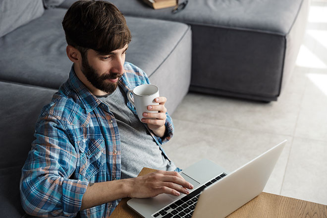 Mann sitzt mit Tasse Kaffee vor dem Laptop